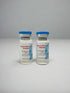 Three vials with blue caps and labels in front of a black box with gold text on a white background